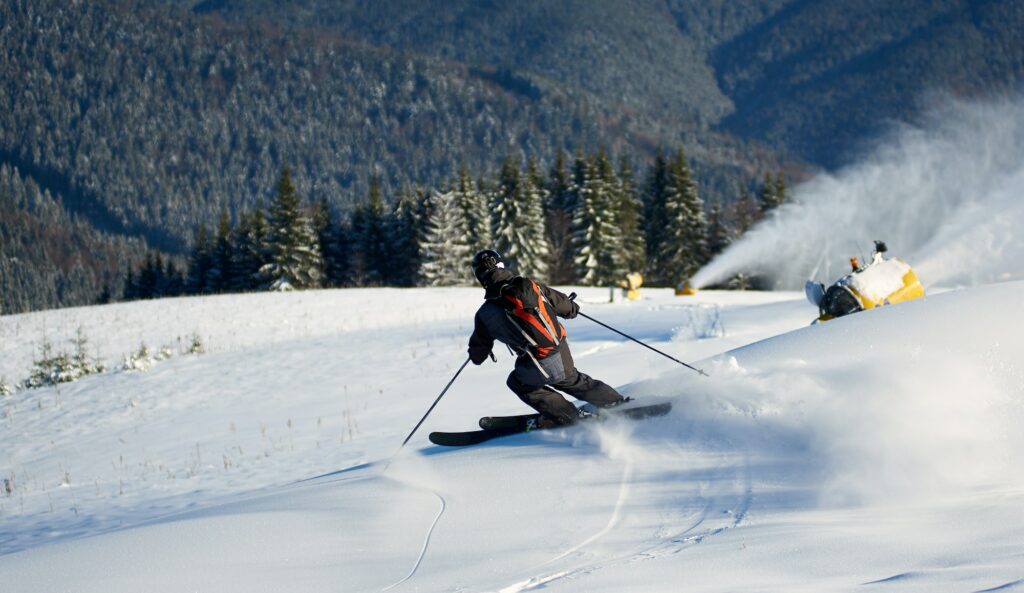 Man skiing on prepared slope with fresh snow. Snow gun machine making artificial snowfall.